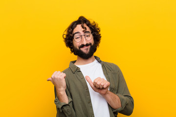 young crazy man smiling cheerfully and casually pointing to copy space on the side, feeling happy...