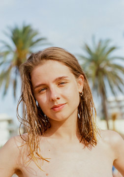  Beautiful Young Blonde Girl Stands In The Sun On The Beach Against Palm Trees, Looks At The Camera And Smiles Mysteriously. Outdoor Portrait Of Naked Lady With Wet Hair On The Sunny Mallorca's Beach