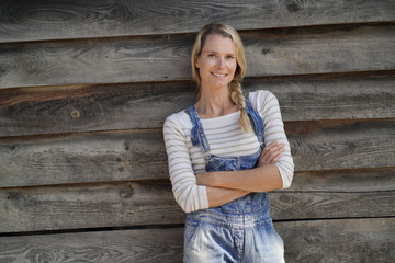 Smiling blond woman with overalls standing in front of barn
