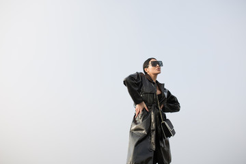 Portrait of a woman in a leather black cloak against the sky. Full height