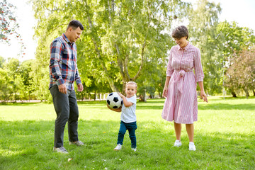 Fototapeta premium family, leisure and people concept - happy mother, father and little son with ball playing soccer at summer park