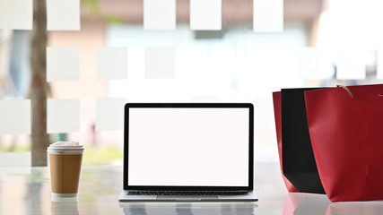 Empty screen laptop computer and shopping bags with coffee on table, Black Friday concept.