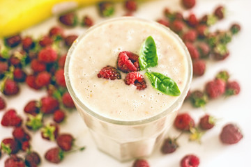 Appetizing milkshake raspberries. Delicious creamy cocktail with fresh berries and banana on blurred white background. Raspberry smoothie with banana and coconut milk. The concept of healthy diet