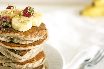 Obraz na płótnie Canvas Delicious banana pancakes on white plate Stack of homemade appetizing fritters with sliced banana and fresh raspberries served on blurred white background