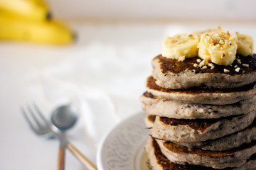 Delicious banana pancakes on white plate. Stack of homemade appetizing fritters with sliced banana served on blurred white background. Coconut Gluten Free Baking.  