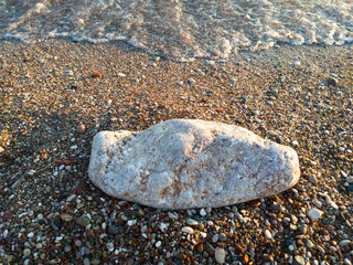An oblong boulder on a beach by the sea. Side lighting reveals the texture of wet sand.