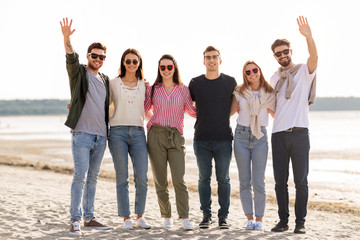 friendship, leisure and people concept - group of happy friends waving hands on beach in summer