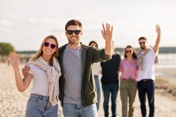 valentine's day, relationships and people concept - happy couple with group of friends on beach in summer waving hands