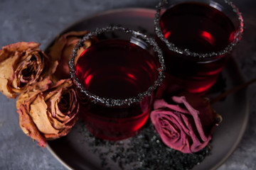 Two glasses with red cocktail, dried rose for Halloween party on the dark background