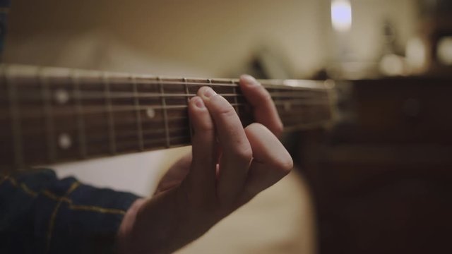 Tilt up shot of the fingers of a guitarist placed on the fret of the mast of the guitar playing a chord doing tapping - closeups of a guitarist practicing