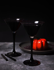 Two glasses with black cocktail, dried roses, pumpkin for Halloween party on the dark background