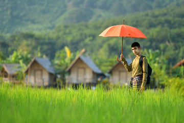Burmese Asians stand on the grass and rice paddies, and Asians use to cover themselves. Behind him is a green field.