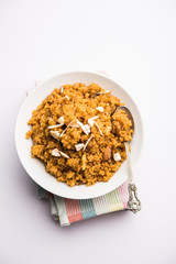 Wheat Laapsi/Lapsi/Shira/Halwa is an Indian sweet dish made of broken wheat or Daliya pieces and ghee along with nuts, raisins and dried fruits. It's a healthy food. served in a bowl, selective focus