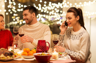 holidays and celebration concept - happy woman calling on smartphone while having christmas dinner with friends at home