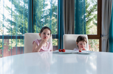 Cute children eating fresh ripe strawberries at home