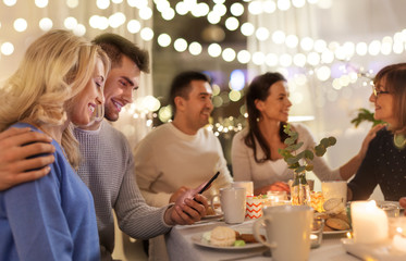 family, holidays and people concept - happy couple with smartphone having tea party at home