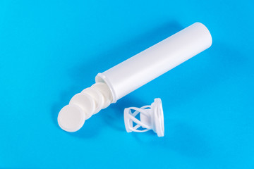 An open white tube with a lid for effervescent tablets lies on the table isolated on a blue background. Pills spill out. copy space. Concept of health, treatment of viral diseases and headaches