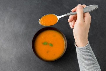 food, eating and new nordic cuisine concept - close up of hands with bowl of pumpkin cream soup and spoon on stone table
