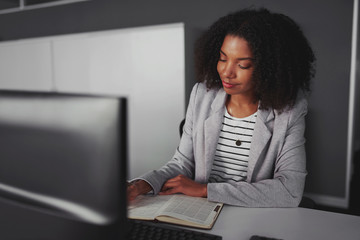 Smiling african american young businesswoman at her desk planning agenda and schedule using calendar event planner - lean in movement