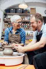 Senior woman spinning clay on a wheel with teacher at pottery class