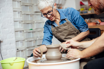 Senior woman spinning clay on a wheel with teacher at pottery class