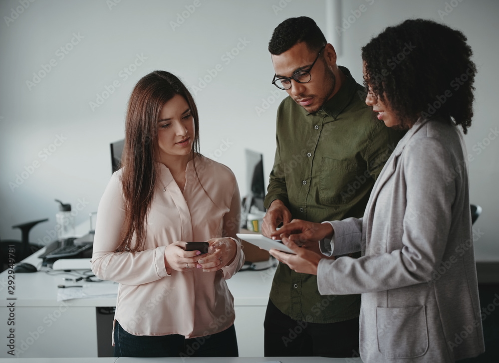 Wall mural Group of multiethnic young concentrated businesspeople using digital tablet at workplace