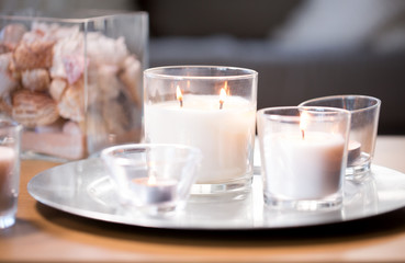 decoration, hygge and cosiness concept - burning white fragrance candles on tray on table