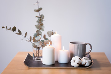 decoration, hygge and cosiness concept - burning white candles, mug, branches of eucalyptus populus and cotton flowers on table © Syda Productions