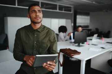Thoughtful young businessman thinking on productive strategy using digital touch pad device in modern office
