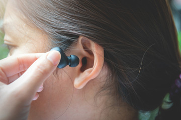Close up of woman is using the black true wireless earbuds by hand to put in ear and control - obrazy, fototapety, plakaty