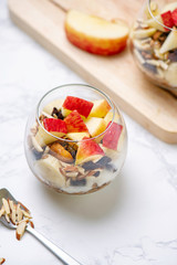 Healthy breakfast of Apple Banana parfaits made with fresh fruit, yogurt and granola over a rustic white table. Selective focus on glass jar. Blurred background and copy space.