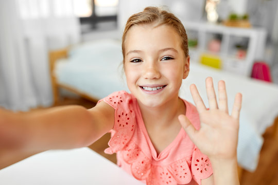 people, children and technology concept - girl taking selfie and waving hand at home