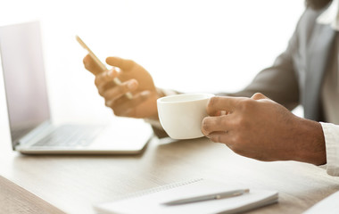 African american ceo drinking coffee and browsing internet on smartphone