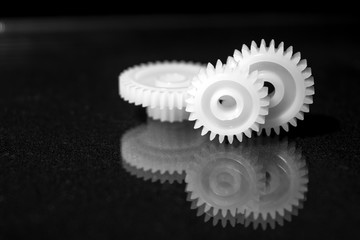 Several white plastic gears on a black mirror background. Mechanical repair. Fix. Reflection. Repair shop. Cogwheels. Elements of a large mechanism. Harmonious work. 