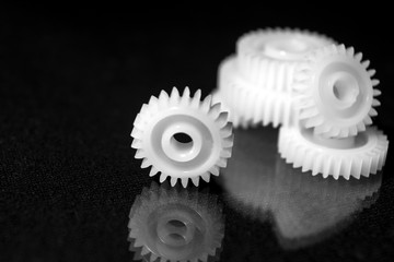 Several white plastic gears on a black mirror background. Mechanical repair. Fix. Reflection. Repair shop. Cogwheels. Elements of a large mechanism. Harmonious work. 