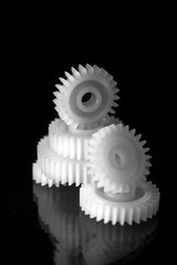 Several white plastic gears on a black mirror background. Mechanical repair. Fix. Reflection. Repair shop. Cogwheels. Elements of a large mechanism. Harmonious work. 