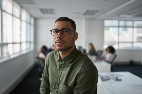 Portrait of a serious young professional businessman wearing eyeglasses looking at camera while colleague at background