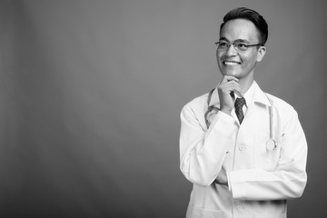 Young handsome Indian man doctor against gray background