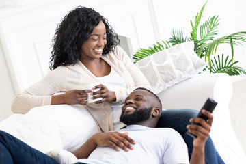 Black family couple relaxing on sofa, spending time at home.