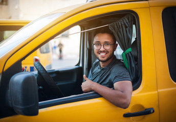 The taxi driver smiles happily, sitting in the cab of a yellow car