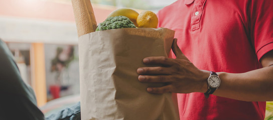 Web banner. smart food delivery service man in red uniform handing fresh food to recipient and young customer receiving order from courier at home, food express delivery and online shopping concept