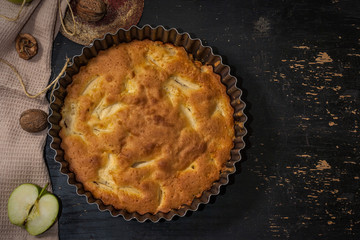 Apple Pie Charlotte on a black wooden table with green apples in iron form.
