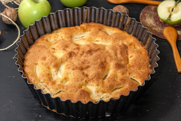 Apple Pie Charlotte on a black wooden table with green apples in iron form.