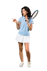 A full-length shot of a Young tennis player woman surprised and pointing side over isolated white background