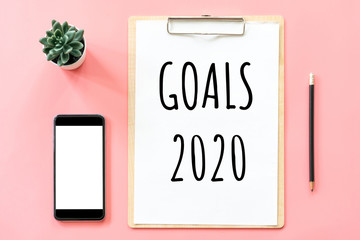 New year concept. Goals 2020 and stationery, blank clipboard, smartphone, pot plant on pink pastel color with copy space