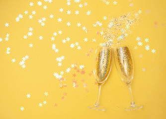 Champagne glasses with gold confetti, glitter yellow background. new year celebration. Top view....
