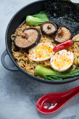 Ramen soup with bok choy and shiitake mushrooms in a cast-iron pan, closeup, vertical shot