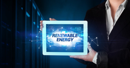 Young business person working on tablet and shows the inscription: RENEWABLE ENERGY