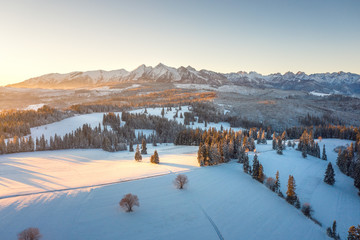 Sunrise in winter mountains. Scenic nature of snowy summits of mountain range illuminated by sun. Aerial view of mountains in sunlight