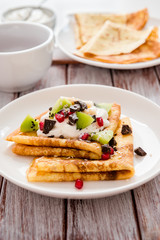 Triangle rolled pancakes with cream, pieces of chocolate, banana, kiwi and pomegranate. Macro view. Tasty thin pancakes